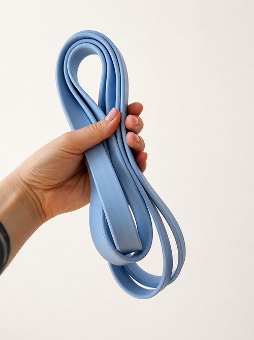 A medium blue resistance loop band held by a person's hand against a plain off-white background.