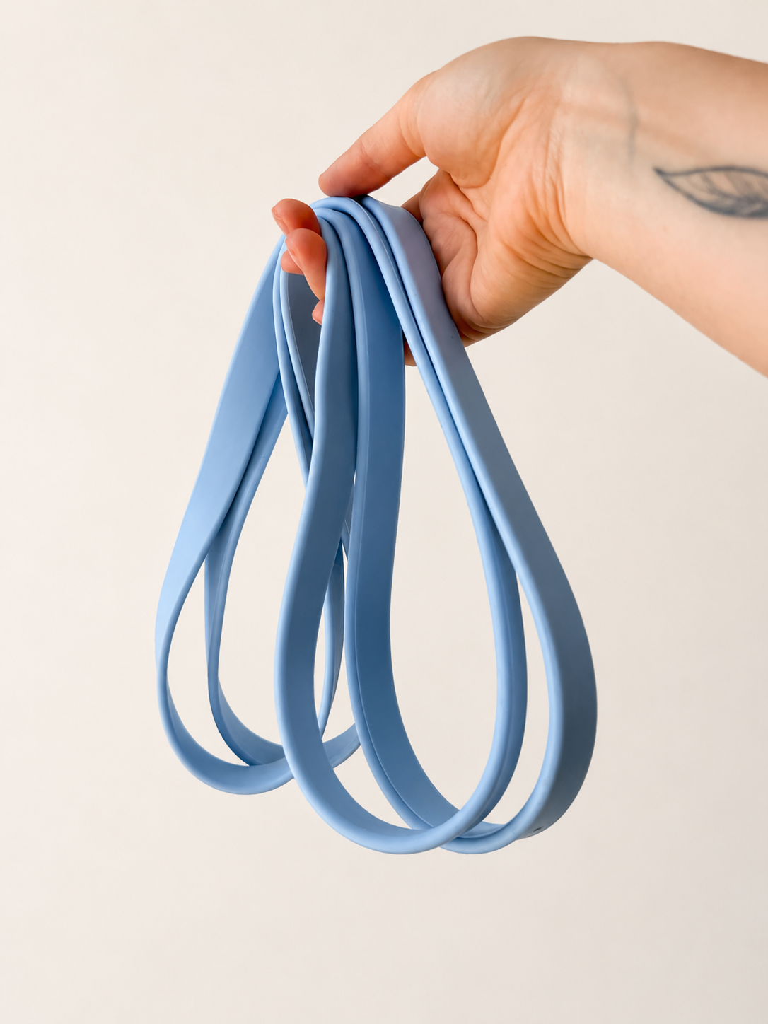 A hand holding a set of medium blue resistance bands against a plain, warm off-white background.