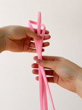 A pair of light silicone loop bands being held by two hands against a plain off-white background.